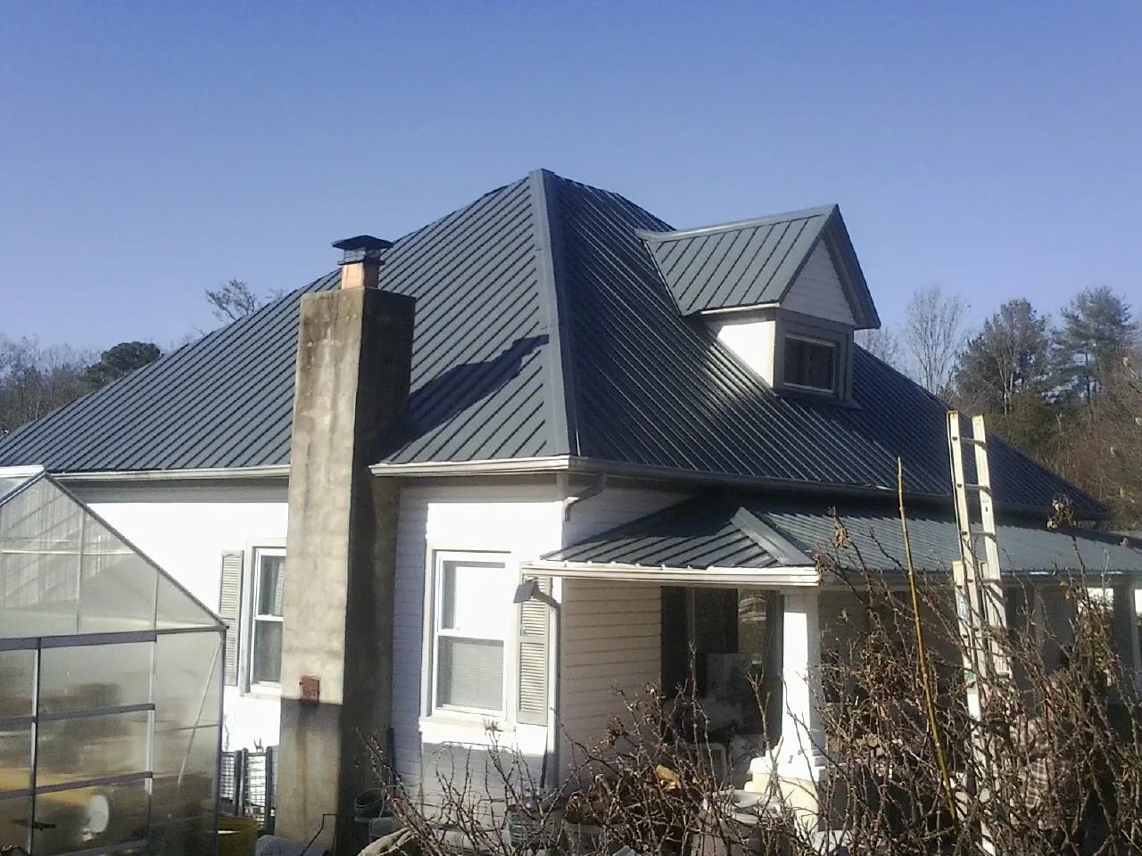 Dark blue standing seam metal roof on a white farmhouse with dormer — Slate & Tile Roof Repair by Roofing Brothers in Mc Leod