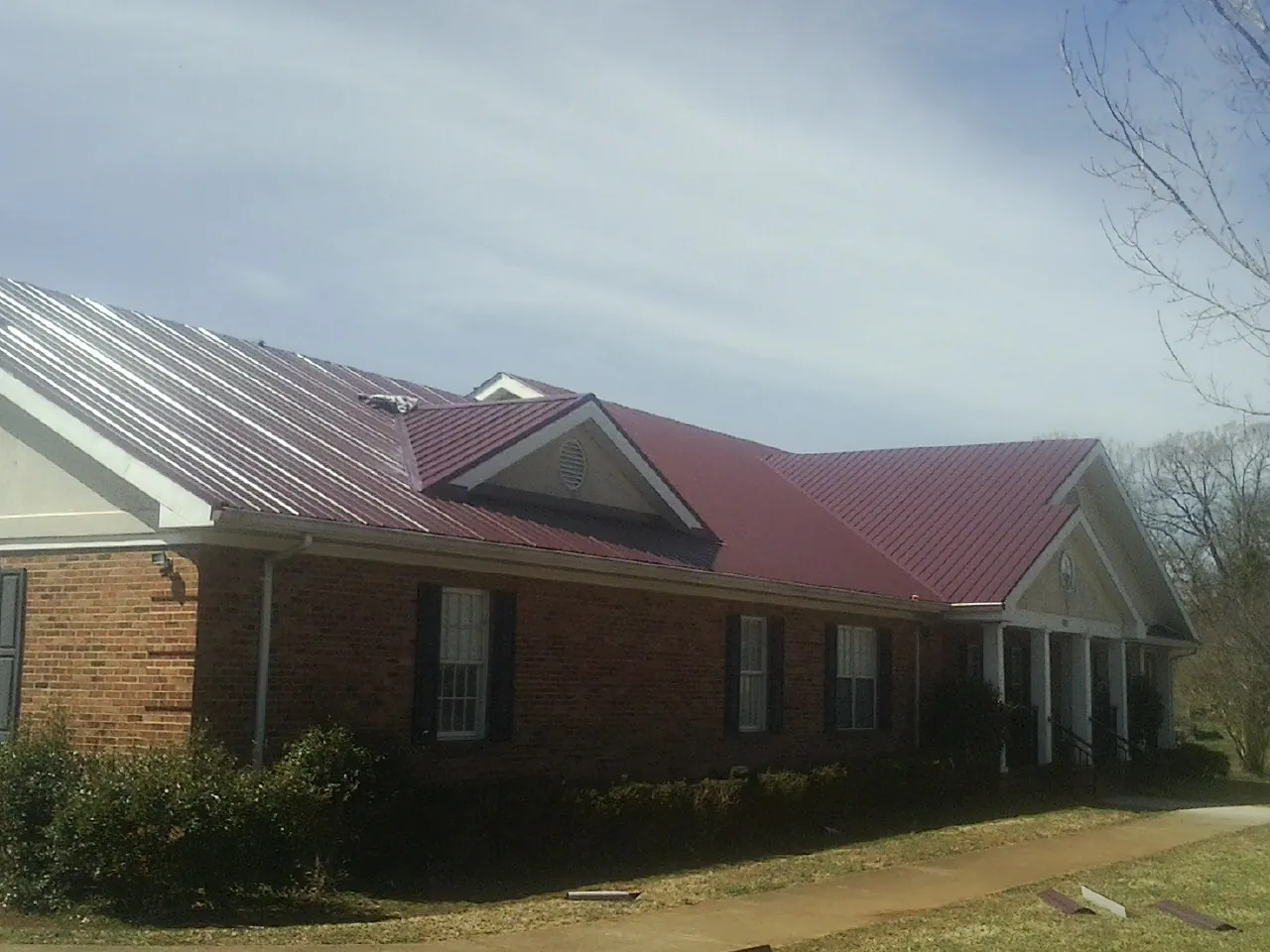 Red metal roof with gabled entries on a long brick building, from a Hail Damage Roof Repair job in Mc Leod