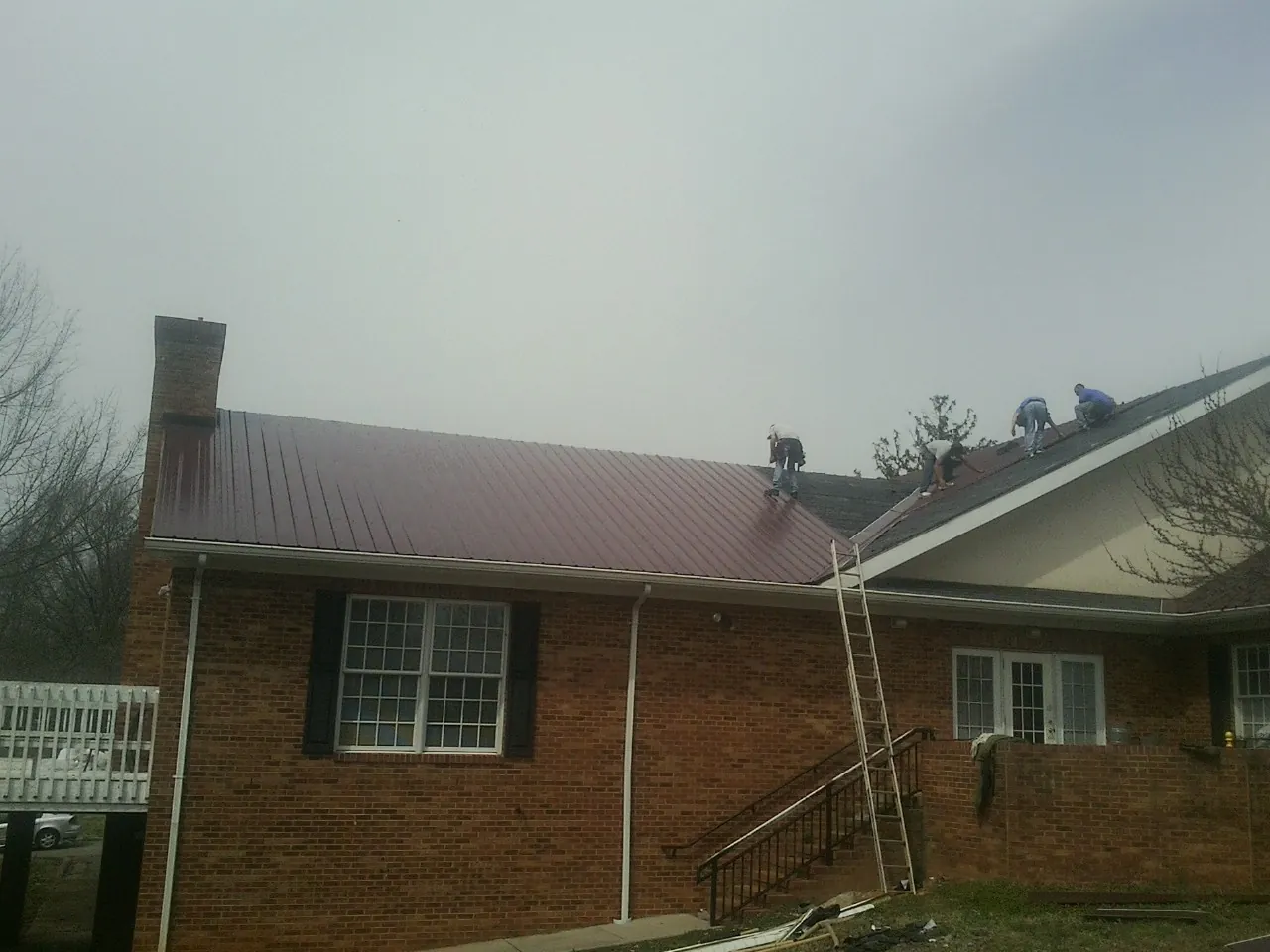 Crew setting red metal roofing panels on a brick home in Mc Leod