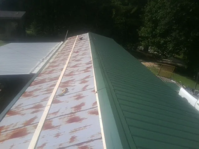 Old rusted panels beside newly installed green metal roofing — Wind Damage Roof Repair by Roofing Brothers in Mc Leod