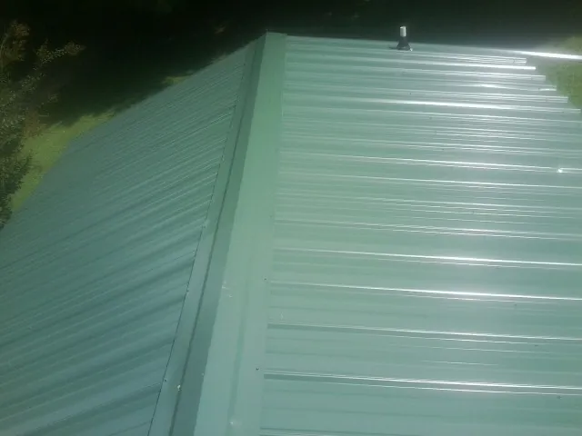 New green metal panels meeting at the ridge of a roof — Flat Roof Repair work by our crew in Mc Leod