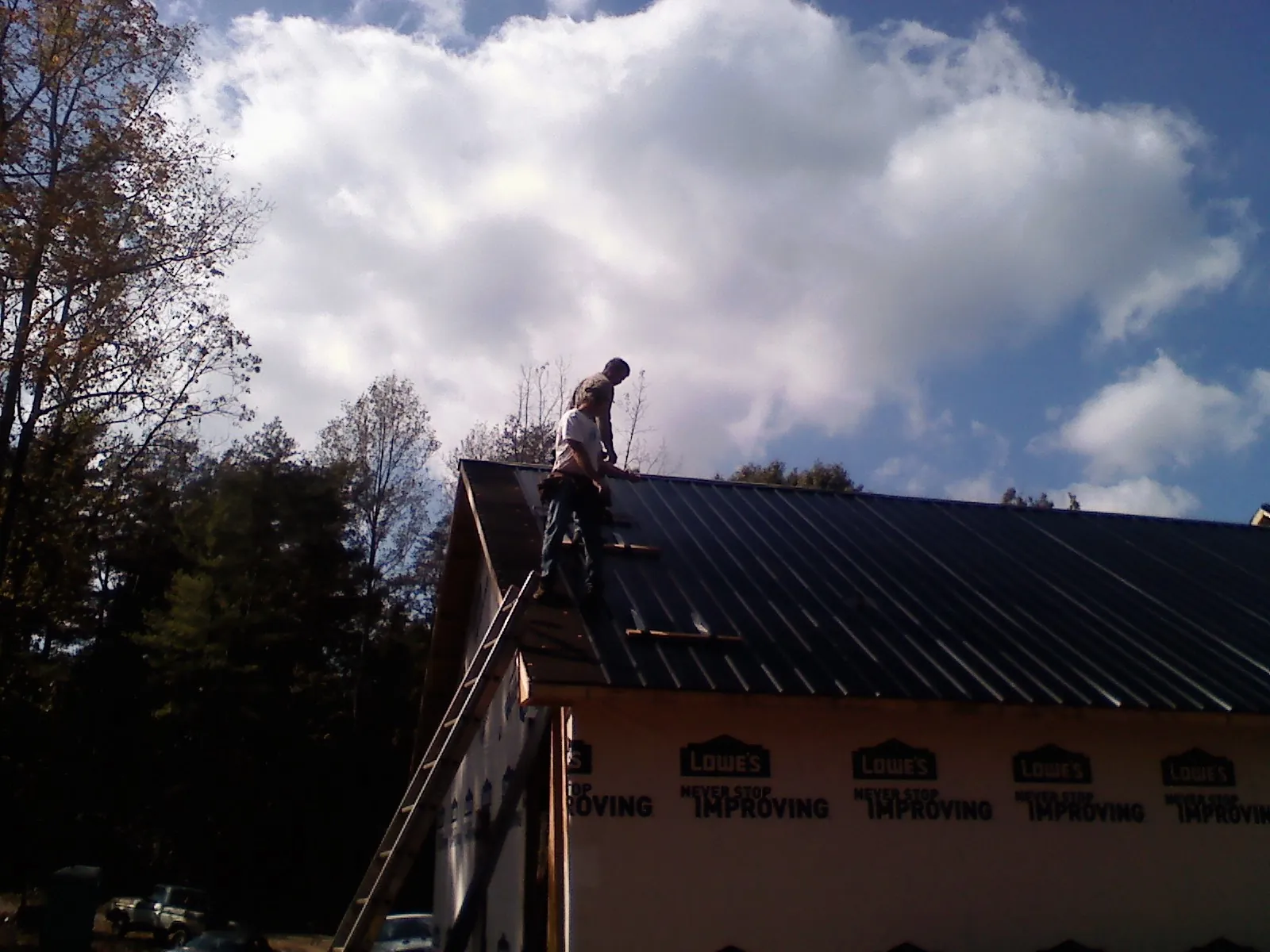 Roofer fastening dark metal panels high against a cloudy sky, from a Roof Inspection job in Mc Leod