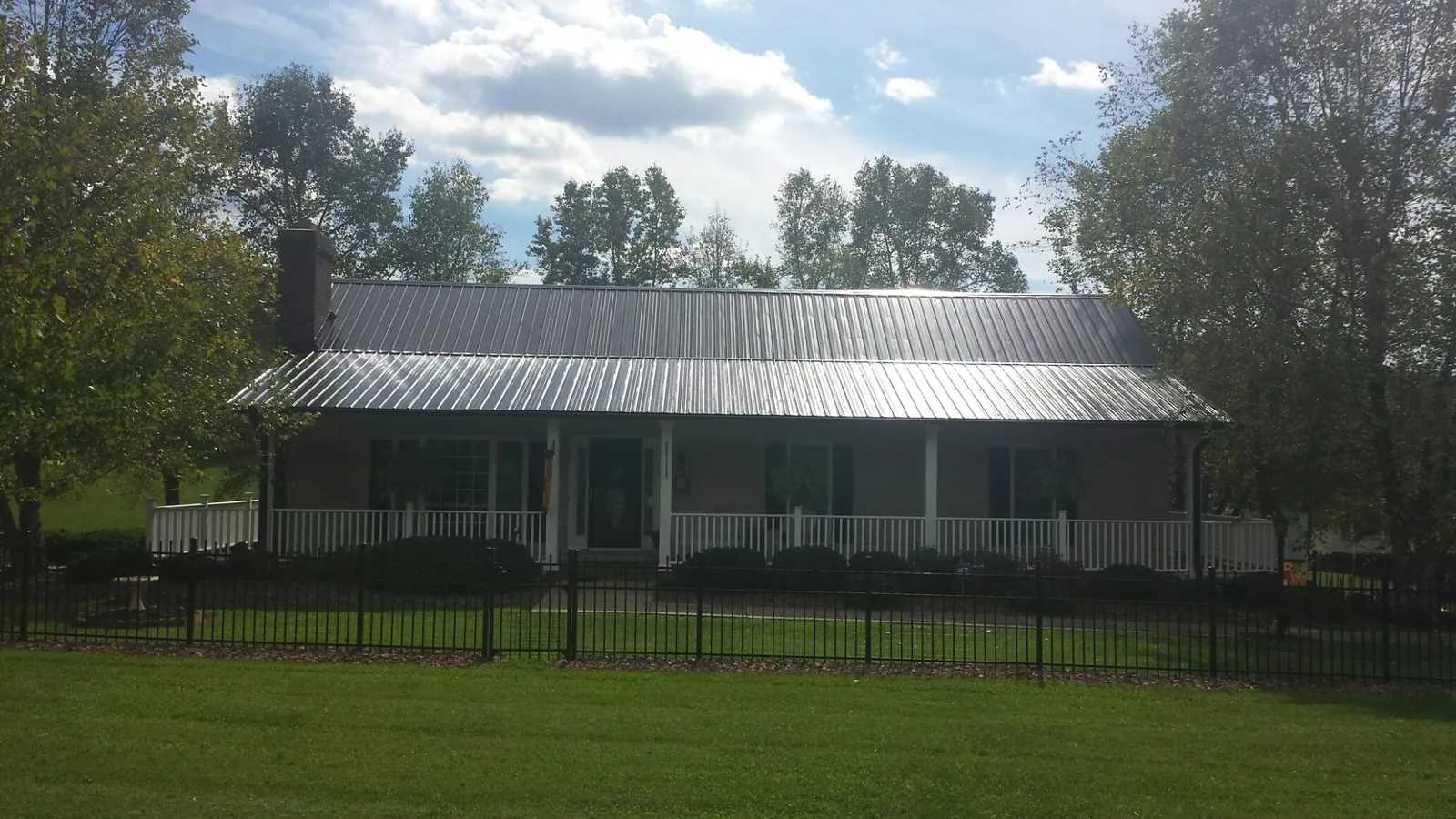 Gray metal roof on a brick ranch with a full width front porch — Gutter Guard Installation work by our crew in Mc Leod