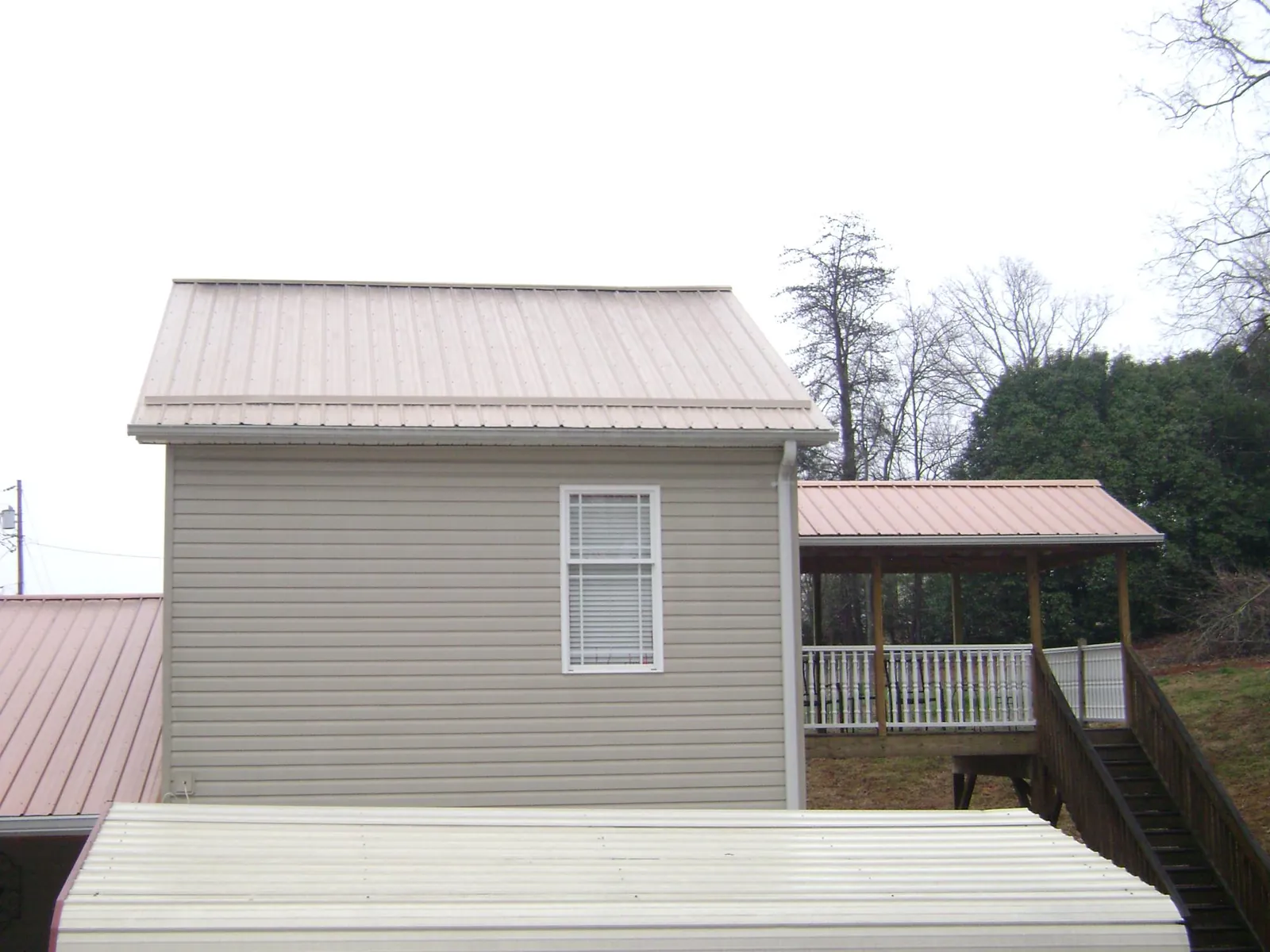 Tan metal roofs on a two story addition and attached porch, from a Roof Replacement job in Mc Leod